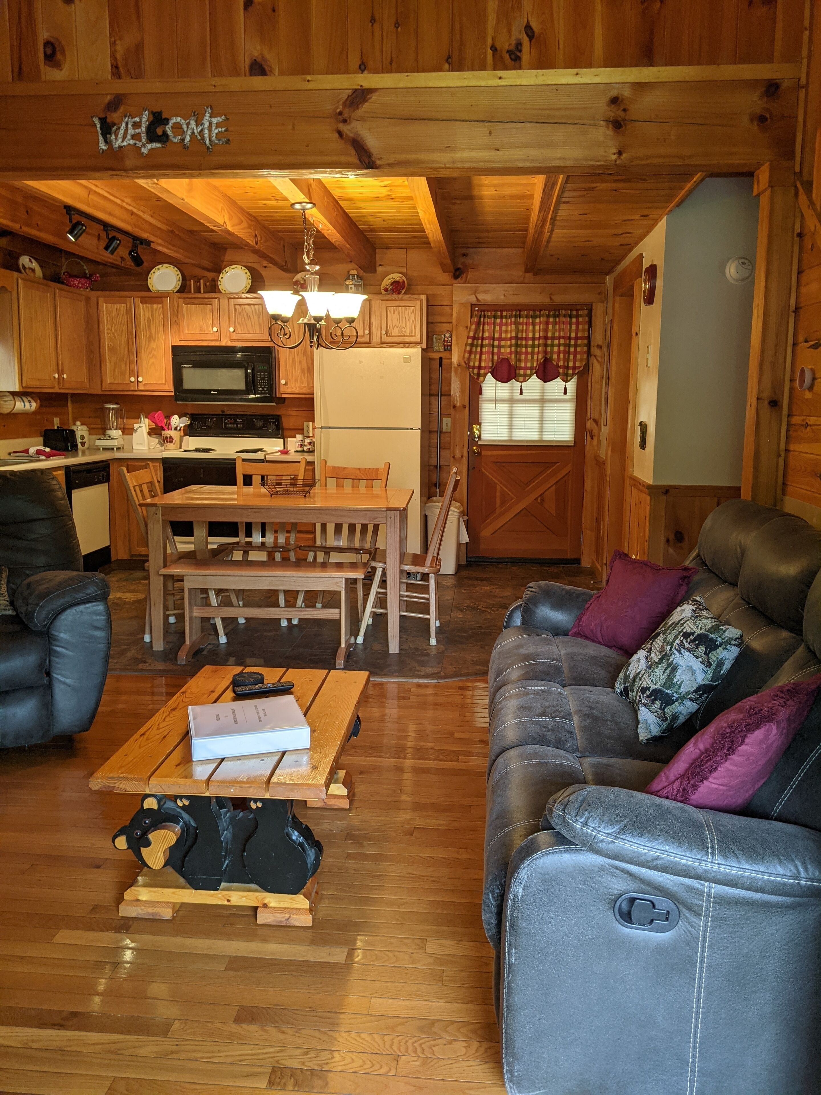 Un intérieur de chalet chaleureux avec des murs en bois, un coin repas, un salon doté de canapés en cuir et une cuisine équipée d’appareils modernes.