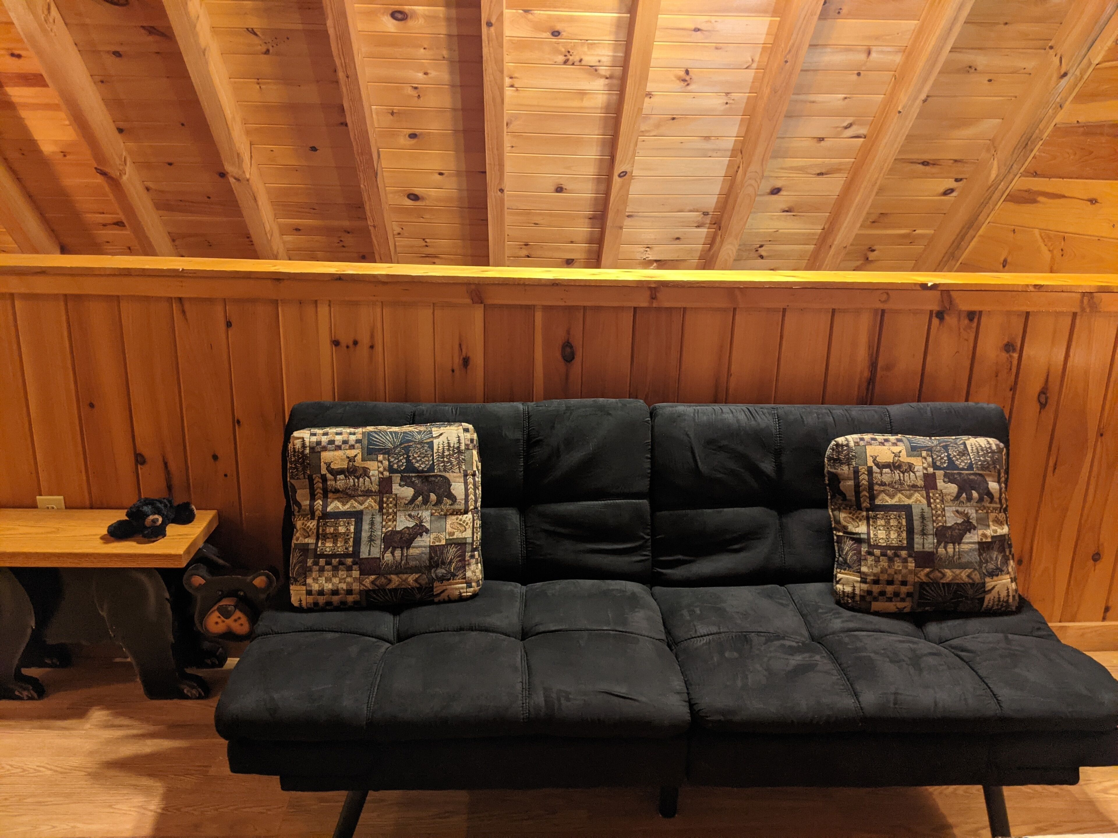 A black leather sofa with patterned cushions against a wooden wall.