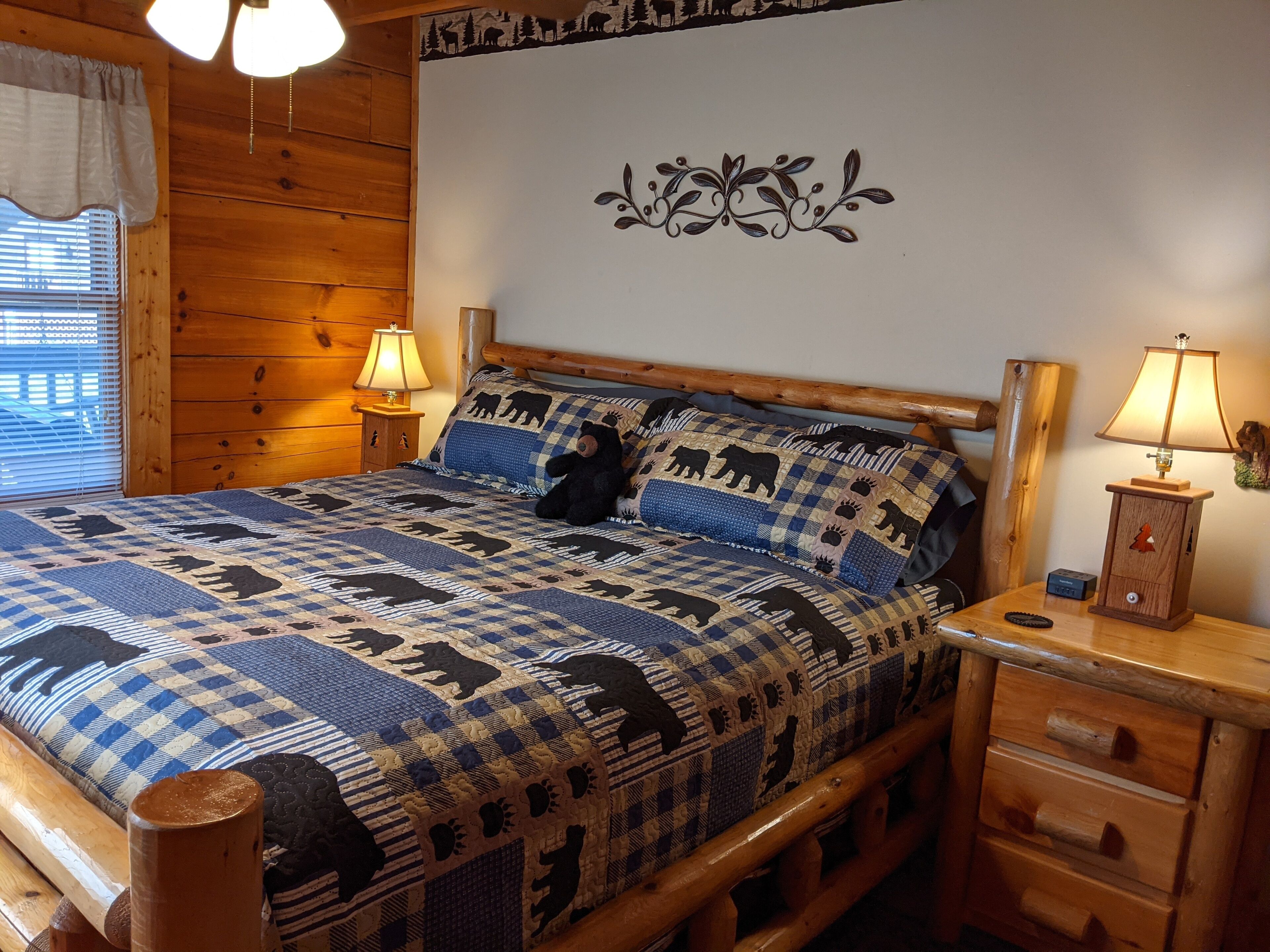 Ein hölzernes Bett mit einer gesteppten Decke mit Tiermotiven, zwei Nachttischlampen und ein kleiner Nachttisch mit Schubladen.