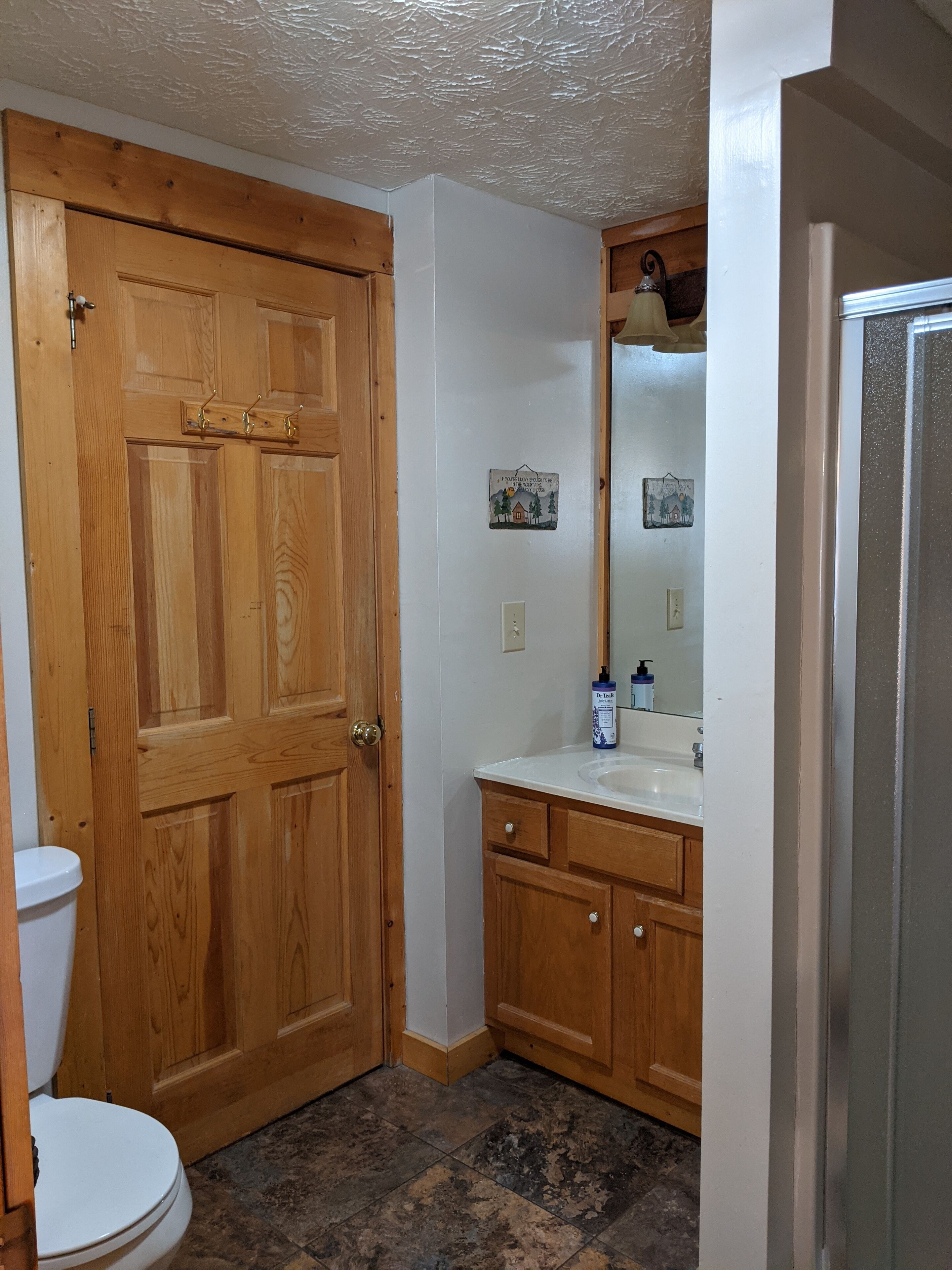 A bathroom with a wooden door, white walls, a sink with a mirror, and a toilet.