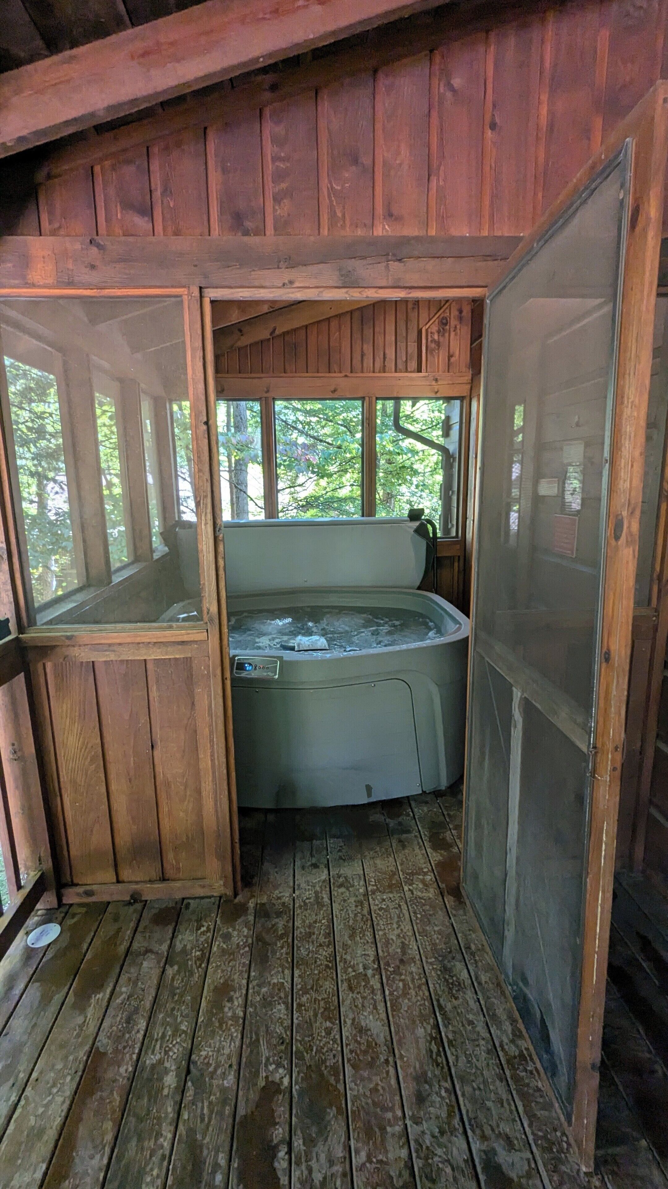 Una cabaña rústica de madera con un jacuzzi en el centro, rodeada de amplios ventanales.