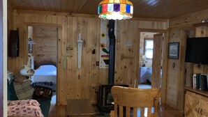 A cozy cabin interior with wooden walls, a wooden ceiling, a colorful stained glass ceiling light, a wooden rocking chair, a small table, a television, and a fireplace. - Beautiful retreat in the Adirondack Park (Malone)