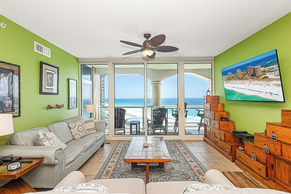 A living room with a sofa, coffee table, and wooden cabinets, a ceiling fan, and a view of the ocean through large glass doors.