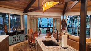 Interior acogedor de una cabaña con cocina, comedor y un gran ventanal con vistas a un bosque.