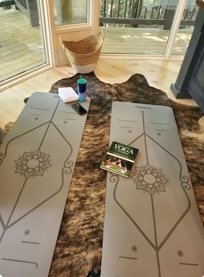 Dos colchonetas de yoga sobre una alfombra de piel, un libro titulado "YOGA para Parejas" y un teléfono inteligente.