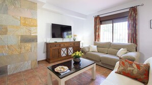 A living room with a stone wall, a flat-screen TV, a wooden cabinet, a sofa, and a coffee table. - Chalet Rocio 1 Conil de la Frontera by Ruralidays (Cádiz)