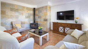 A living room with a stone wall, a fireplace, a TV, and a wooden cabinet. - Chalet Rocio 1 Conil de la Frontera by Ruralidays (Cádiz)
