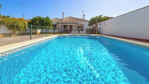 A rectangular swimming pool with clear blue water, surrounded by a white wall and a fence.