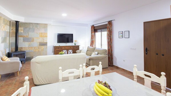 A cozy living room with a sofa, a TV, a fireplace, and a dining area with a table and chairs.