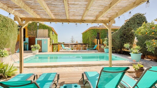 Een zwembadgedeelte met houten pergola’s, ligbedden en potplanten.