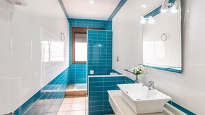 A modern bathroom with white and blue tiles, a large mirror, a sink, and a shower area. - Chalet Rocio 2 Conil de la Frontera by Ruralidays (Cádiz)