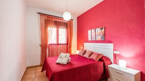 A bedroom with a red bedspread, a white nightstand, and a painting on the wall. - Chalet Rocio 2 Conil de la Frontera by Ruralidays (Cádiz)