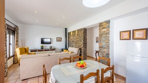 A modern living room with a sofa, a dining table with chairs, a TV, and a refrigerator. - Chalet Rocio 2 Conil de la Frontera by Ruralidays (Cádiz)