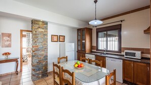 A compact kitchen with a dining table, a refrigerator, a microwave, and wooden cabinets. - Chalet Rocio 2 Conil de la Frontera by Ruralidays (Cádiz)