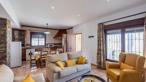 A living room with a sofa, armchair, and coffee table. There is a kitchen area with a dining table and chairs. - Chalet Rocio 2 Conil de la Frontera by Ruralidays (Cádiz)