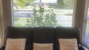 A brown leather sofa with two white pillows, one with the text "be our guest," and a framed sign above reading "BE OUR GUEST whether you come in to visit, or just to rest, when you enter our home you will be blessed."
