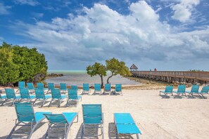 A beach with rows of blue lounge chairs and a wooden pier extending into the water.