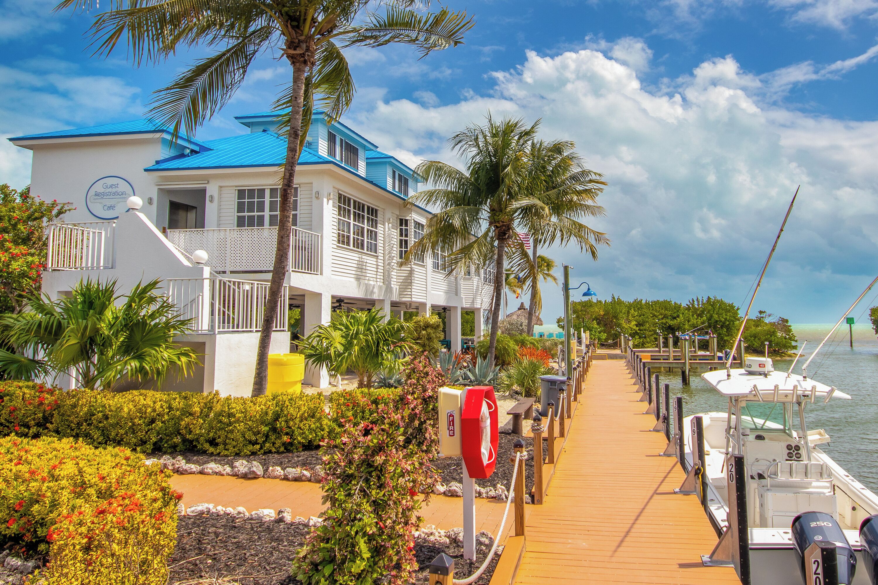 A coastal hotel with a blue roof, a guest registration area, and a dock with boats.