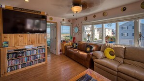 A cozy living room with a wooden bookshelf, leather sofa, and a large TV. - 6 Bedroom Home 3rd off Beach with Ocean & Bay View HotTub +++ (Long Beach)