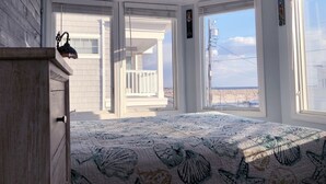 A bedroom with a large bed, a wooden dresser, and a view of the beach through a bay window. - 6 Bedroom Home 3rd off Beach with Ocean & Bay View HotTub +++ (Long Beach)