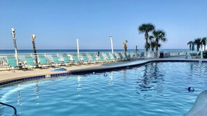 Une piscine avec vue sur l’océan, entourée de chaises longues et de palmiers.