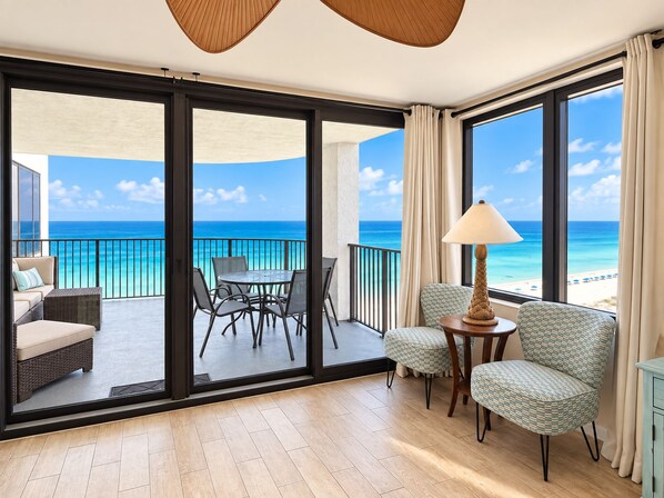 A room with a view of the ocean, a table with chairs, a sofa, and a lamp.