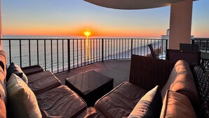 Un balcon offrant une vue sur le coucher de soleil sur l’océan, aménagé avec des canapés en cuir et une petite table.