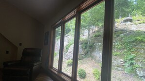 A room with a large window, a wooden floor, and a dark-colored chair. - Rock Hill Retreat- a home with natural stone formations at every turn!  (Rockbridge)
