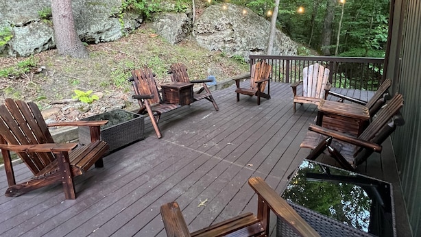 A wooden deck with Adirondack chairs and a small table, surrounded by trees and string lights. - Rock Hill Retreat- a home with natural stone formations at every turn!  (Rockbridge)