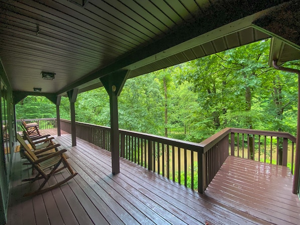 Une terrasse en bois avec des fauteuils à bascule, un espace abrité et une vue sur une forêt.