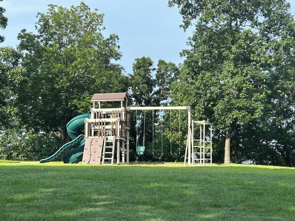 Un parque infantil con un tobogán y estructuras para escalar, rodeado de árboles.