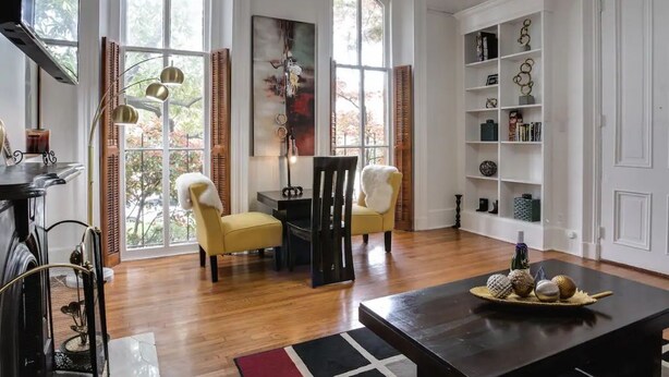 A spacious living room with large windows, a fireplace, a coffee table with decorative items, and a bookshelf. - Downtown Memphis 2 BR Eleanor Rigby suite Apt 101 (Memphis)