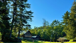 A large log cabin with a metal roof, surrounded by dense trees and a well-maintained lawn. - Log Haven Cabin, Gore Skiing, Pool/AC/Fireplace, Steps to Loon Lake (Chestertown)