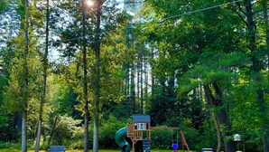 A playground with a slide, swings, and a small wooden structure. - Log Haven Cabin, Gore Skiing, Pool/AC/Fireplace, Steps to Loon Lake (Chestertown)