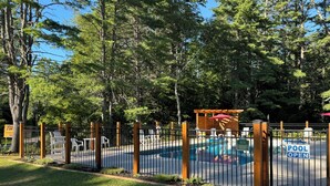 A fenced pool area with a wooden pergola and a sign indicating the pool is open. - Log Haven Cabin, Gore Skiing, Pool/AC/Fireplace, Steps to Loon Lake (Chestertown)