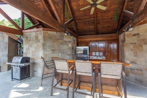 An outdoor kitchen area with stone walls, a grill, a refrigerator, and bar stools. - Ma & Pa’s BeeHive Condo (Pigeon Forge)