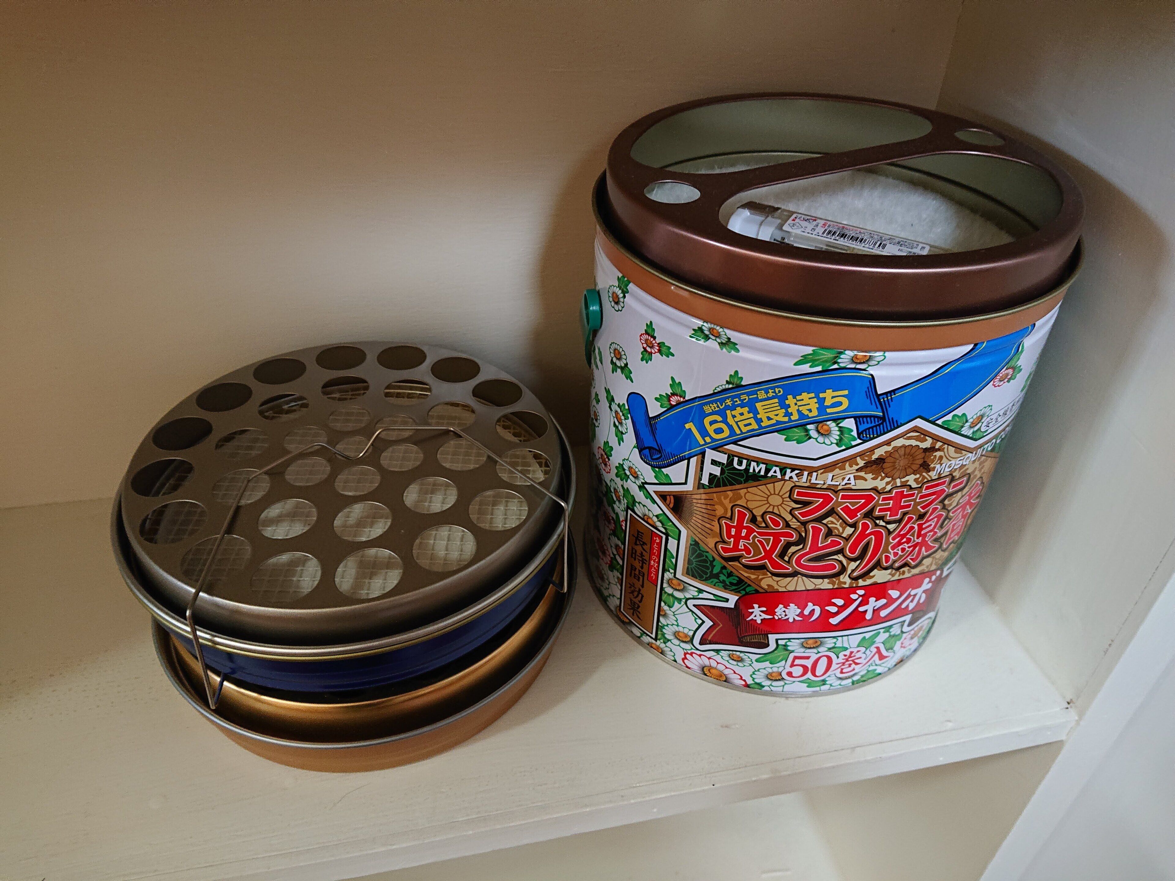 A shelf with a metal container with a perforated lid and a cylindrical canister with a label.