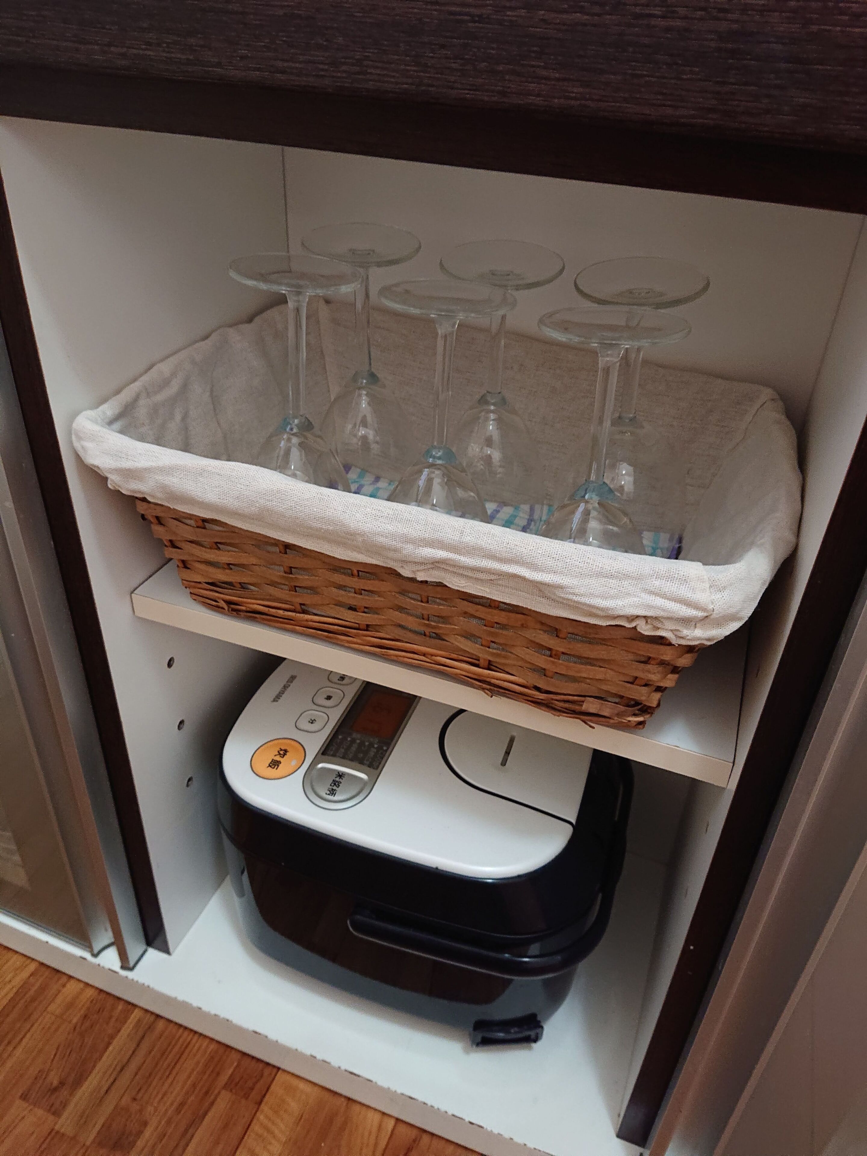 A kitchen with a coffee machine, a basket of wine glasses, and a white cloth.