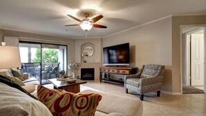 Uma sala de estar com ventilador de teto, lareira, televisão e poltrona estampada.