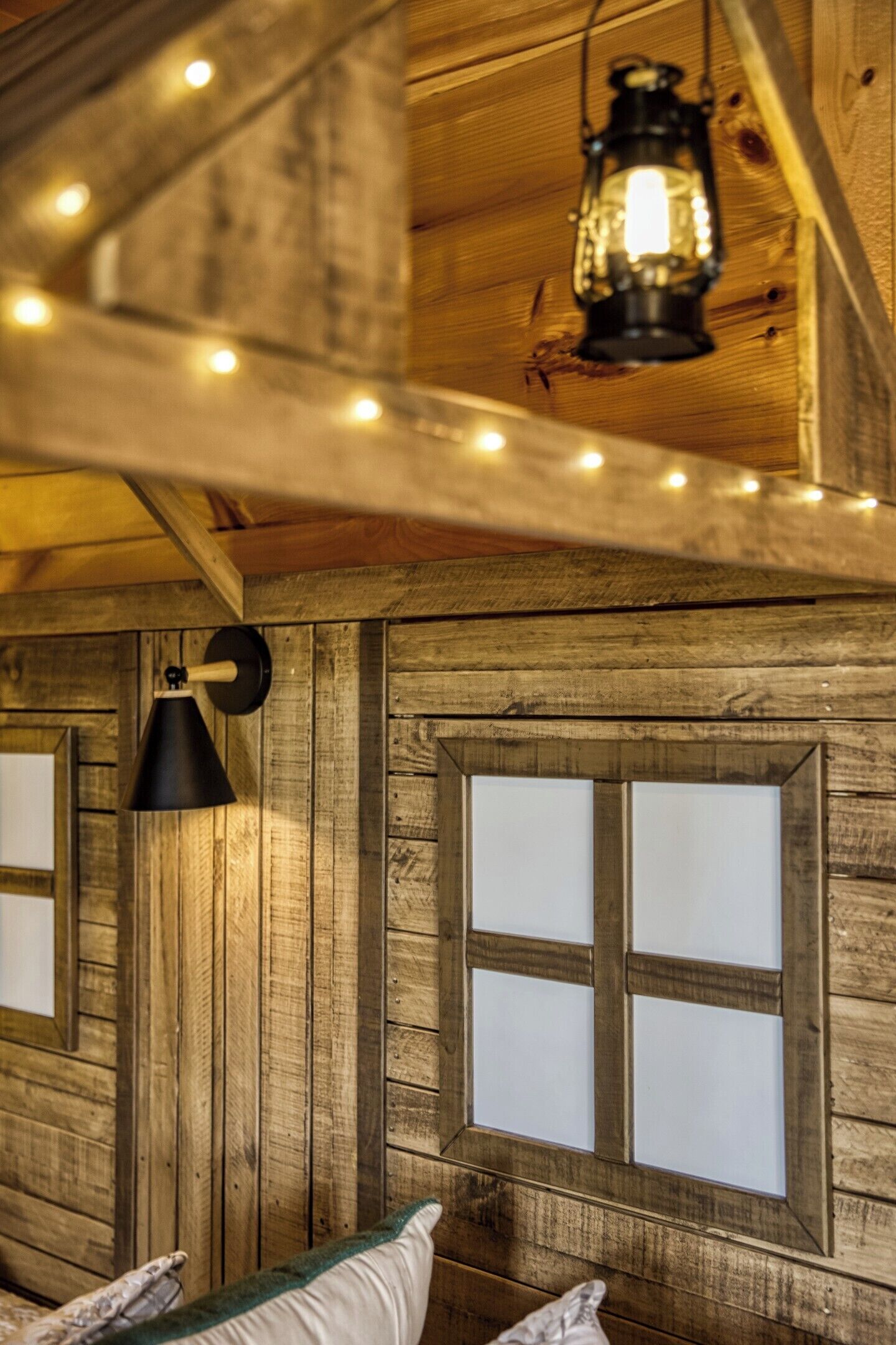L’intérieur d’un chalet rustique en bois, avec un lit, une lanterne suspendue et des guirlandes lumineuses.