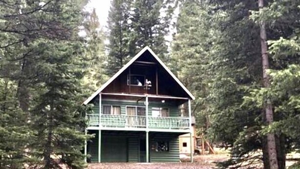 A two-story cabin with a balcony, surrounded by tall pine trees.