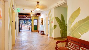 A hotel corridor with tiled flooring, a wooden bench, and a wall with a large leaf mural.