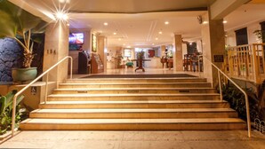 A hotel lobby with a marble staircase, a reception desk, and a large potted plant.