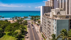A hotel with a view of the ocean, a street with cars, and palm trees.