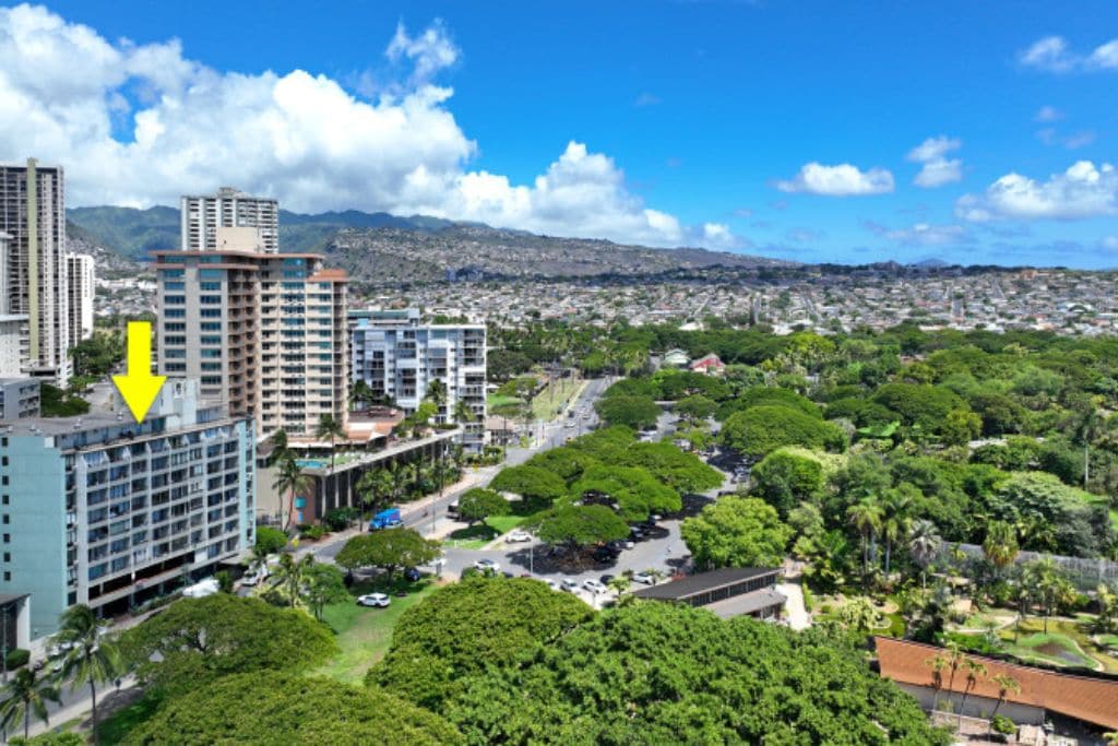 Un hôtel de grande hauteur, avec de nombreux étages, entouré d’une végétation luxuriante et offrant une vue sur un paysage urbain avec des montagnes en arrière-plan.