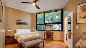 A bedroom with a bed, a chair, a desk, a ceiling fan, and a window with a view of trees.