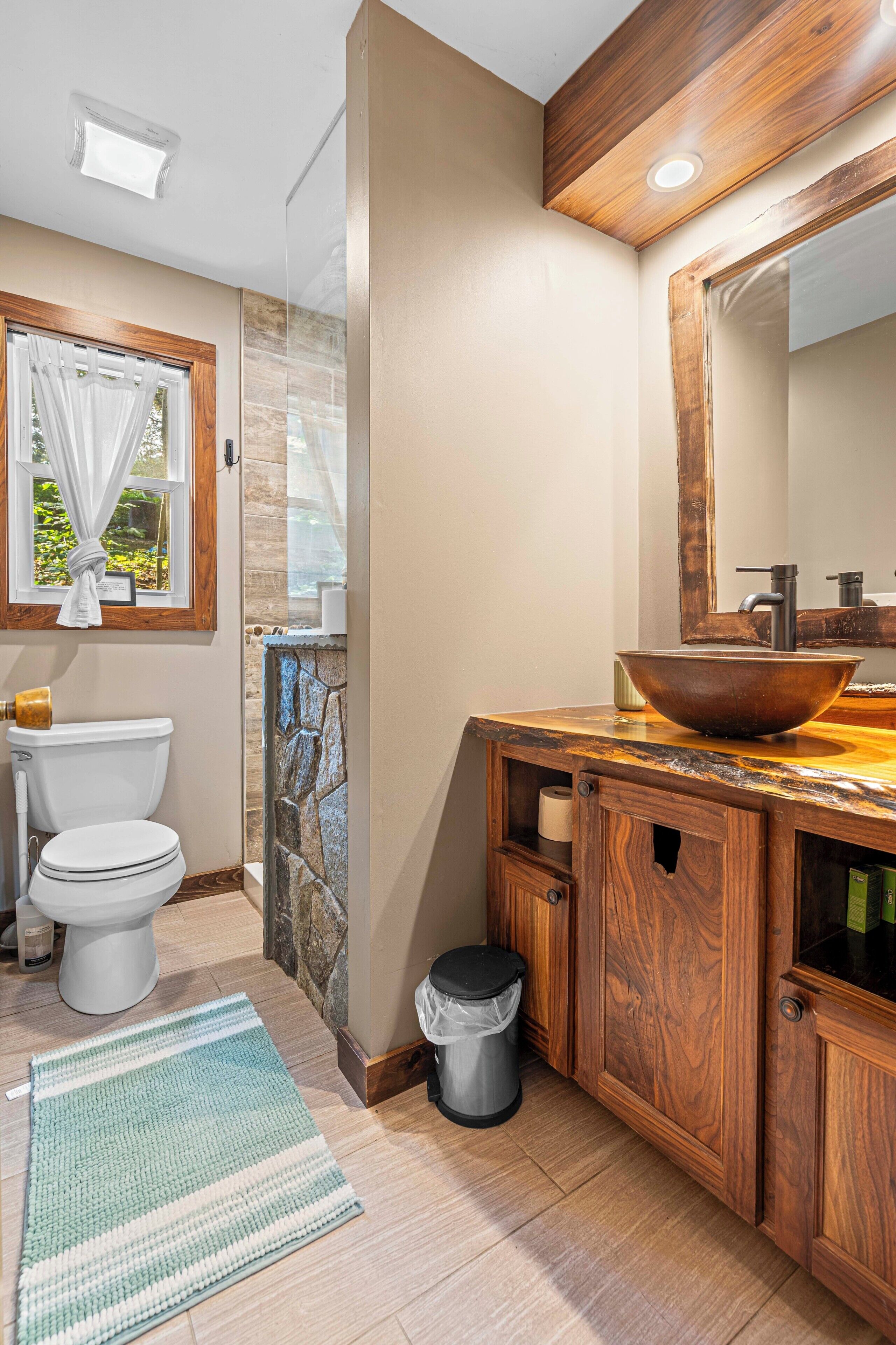 Ein Badezimmer mit Toilette, einem Waschbecken aus Holz, einem Spiegel und einer Wand mit Steinverkleidung.