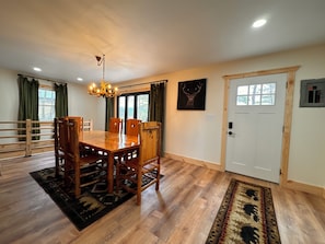 A dining area with a wooden table and chairs, a chandelier, and a rug.