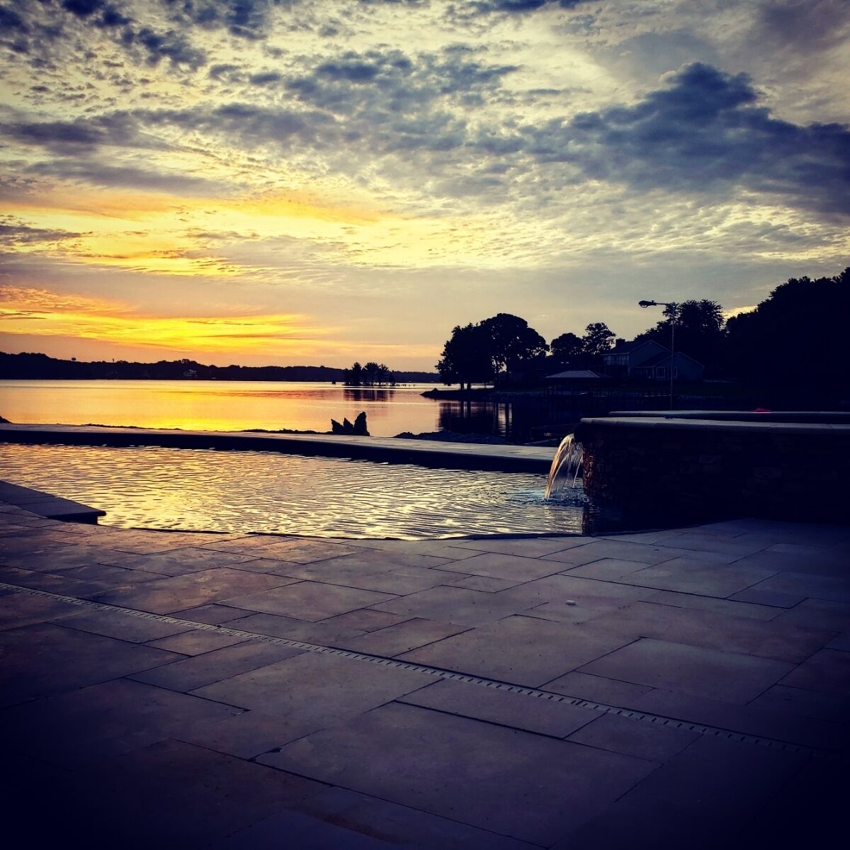 Une vue sur le coucher de soleil, avec un plan d’eau calme et un sentier de pierres menant à un quai.