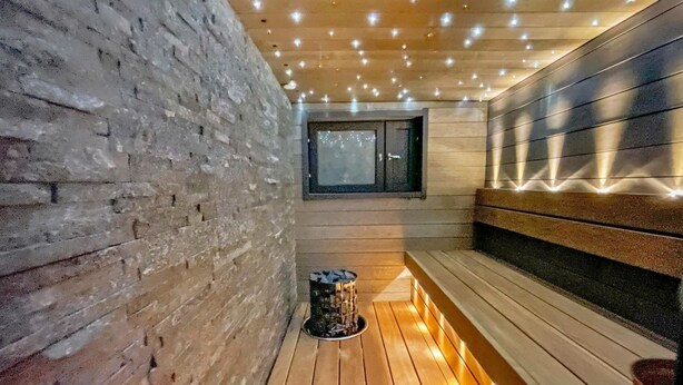 Eine Sauna mit Holzbänken, einer Ziegelwand und einer mit Lampen versehenen Decke.
